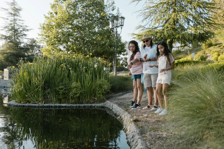 a group of people standing next to a pond, family friendly, pièce de résistance, see fishes swimming, summer lighting