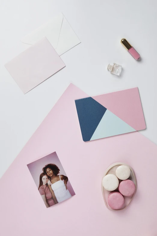 a pink table topped with pink macarons and photos, a picture, inspired by Malevich, trending on pexels, color field, pair of keycards on table, pastel palette silhouette, layered paper style, pink and blue