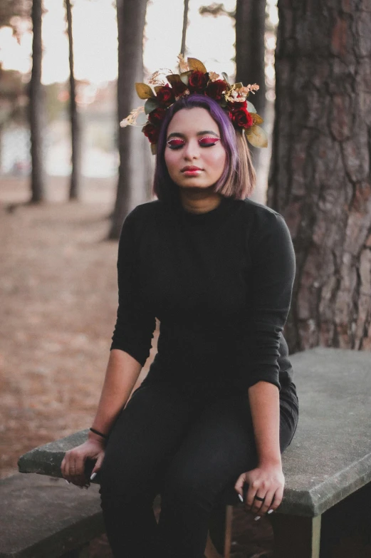 a woman sitting on a bench with a flower crown on her head, a colorized photo, inspired by Elsa Bleda, pexels contest winner, wearing a black sweater, black and purple hair, 🍂 cute, infp young woman