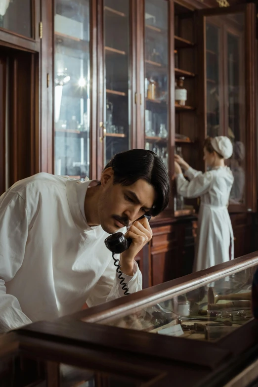 a man standing in front of a glass case talking on a phone, inspired by Nikolai Ge, trending on pexels, art nouveau, nurse, ! movie scene, dressed as a pastry chef, romanian heritage