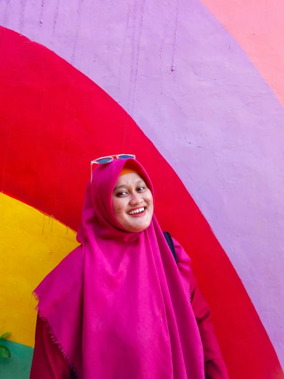 a woman standing in front of a rainbow painted wall, inspired by JoWOnder, pexels contest winner, sumatraism, hijab, ((pink)), smiling, movie photo