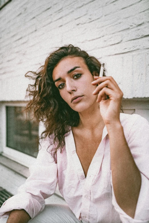 a woman sitting on a window sill talking on a cell phone, an album cover, trending on pexels, antipodeans, with a cigarette in its mouth, halfbody headshot, slightly tanned, arian mark