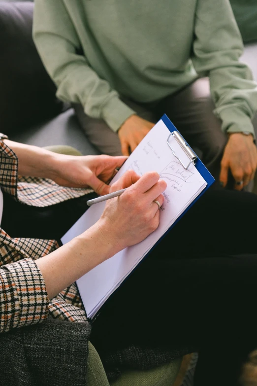 a woman sitting on a couch holding a clipboard, pexels, séance, a person standing in front of a, mental health, pen and paper