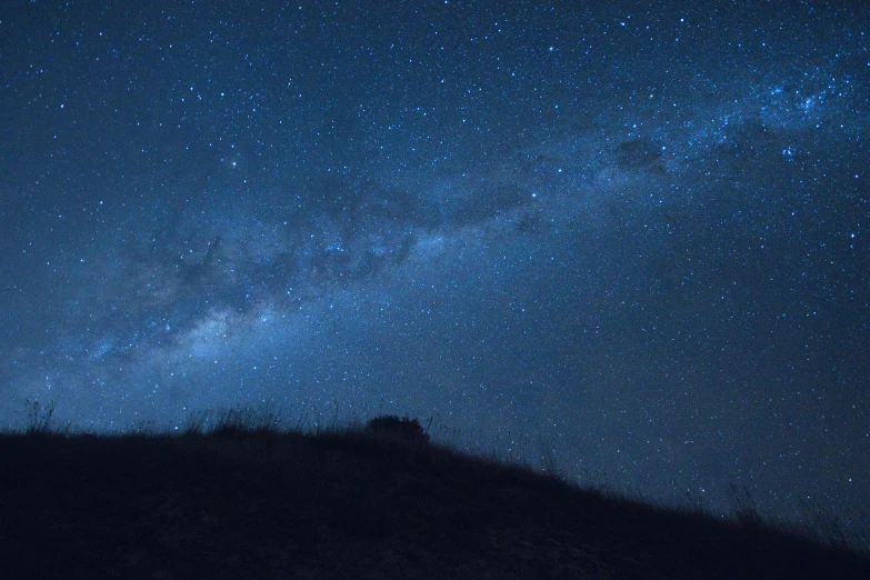 a person standing on top of a hill under a night sky, pexels contest winner, minimalism, the milk way up above, southern cross, panorama, blue