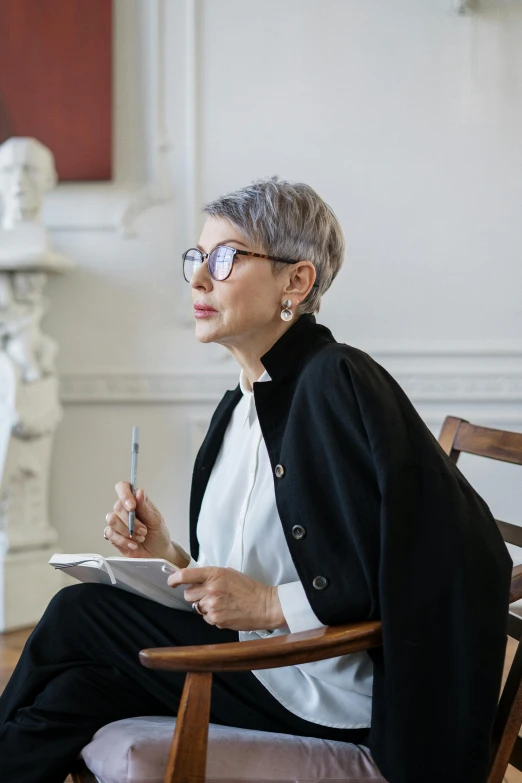 a woman sitting in a chair writing on a piece of paper, inspired by Ruth Jên, trending on pexels, visual art, short silver hair, portrait of a museum art curator, marie - gabrielle capet style, androgynous male