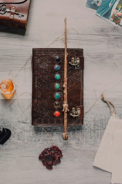 a brown book sitting on top of a wooden table, long trunk holding a wand, embedded with gemstones, flatlay, casting spells