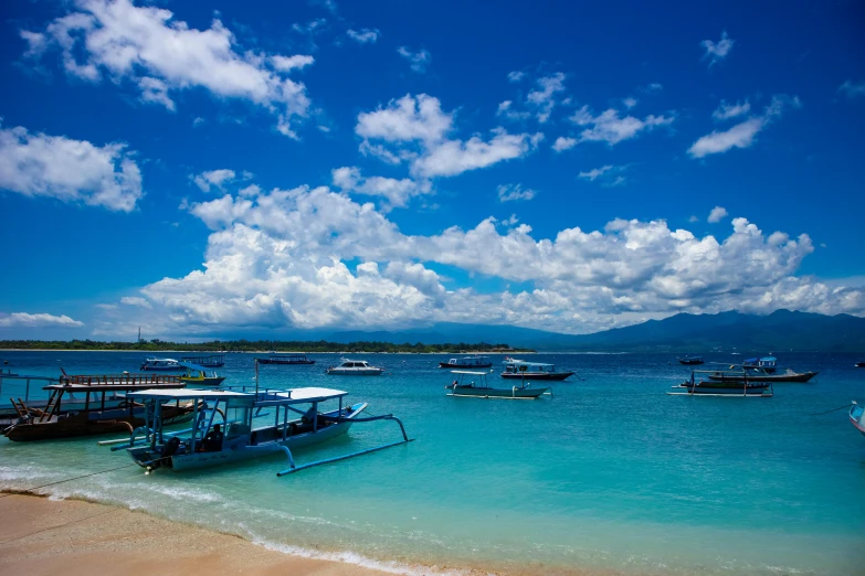 a group of boats sitting on top of a sandy beach, blue water, avatar image, under blue clouds, jakarta