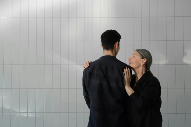 a man and a woman standing next to each other, by Emma Andijewska, unsplash, bauhaus, wearing a grey robe, showers, embracing, caretaker