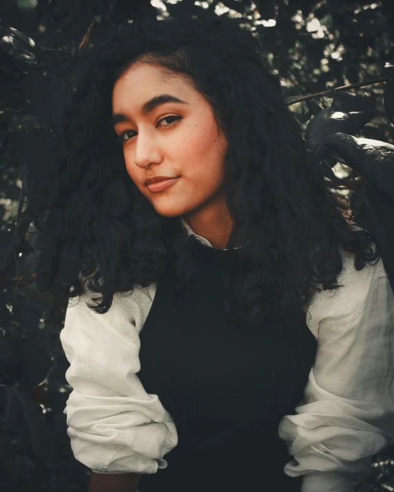 a woman with long black hair standing in front of a tree, inspired by irakli nadar, trending on unsplash, sumatraism, curly bangs, portrait androgynous girl, she is about 1 6 years old, she has olive brown skin