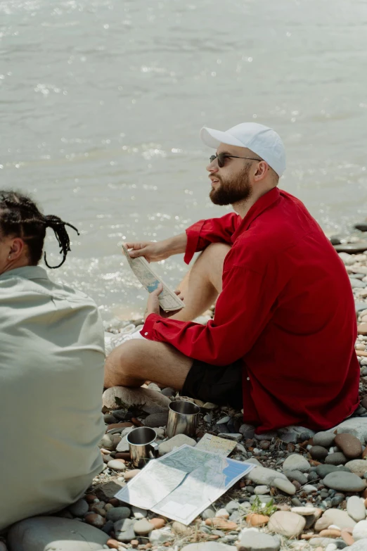 a couple of men sitting on top of a rocky beach, mac miller, on a riverbank, wearing red clothes, snacks
