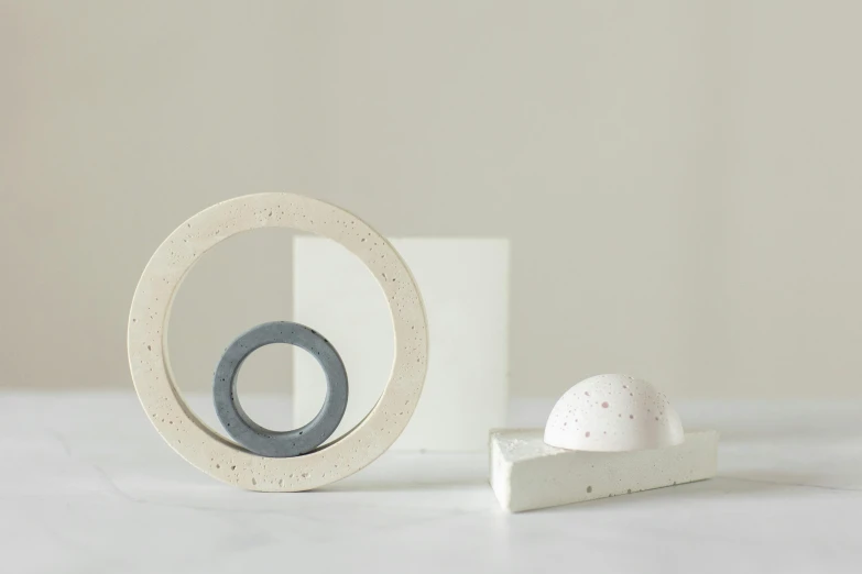a close up of a white object on a table, an abstract sculpture, inspired by Rachel Whiteread, featured on pinterest, new sculpture, orbital rings, inside a frame on a tiled wall, miniature product photo, concrete )