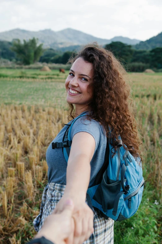 a man and a woman holding hands in a field, brown curly hair, with a backpack, waving at the camera, giorgia meloni