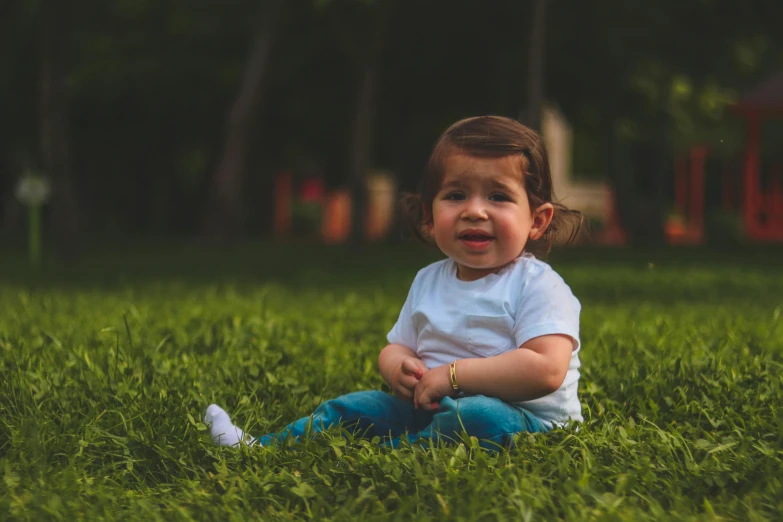 a little girl sitting on top of a lush green field, by Attila Meszlenyi, pexels contest winner, handsome, sitting cross-legged, frowning, toddler