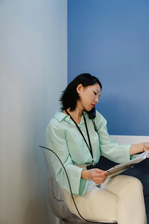 a woman sitting on a chair reading a paper, healthcare worker, asian descent, wearing a light blue shirt, large)}]