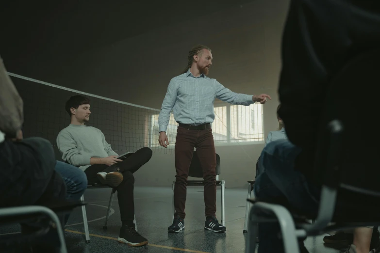 a man standing in front of a group of people, sitting on a chair