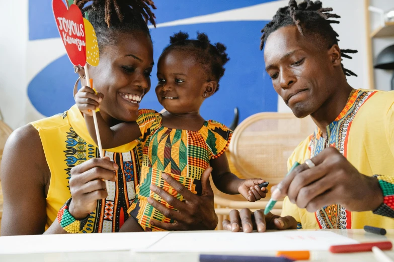 a man and woman sitting at a table with a child, by Ingrida Kadaka, pexels contest winner, black arts movement, holding a paintbrush in his hand, a brightly colored, celebrating, ikea