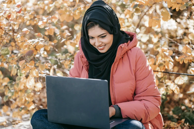 a woman sitting on a bench using a laptop, inspired by Maryam Hashemi, trending on pexels, hurufiyya, wrapped in a black scarf, warm coloured, teaching, student