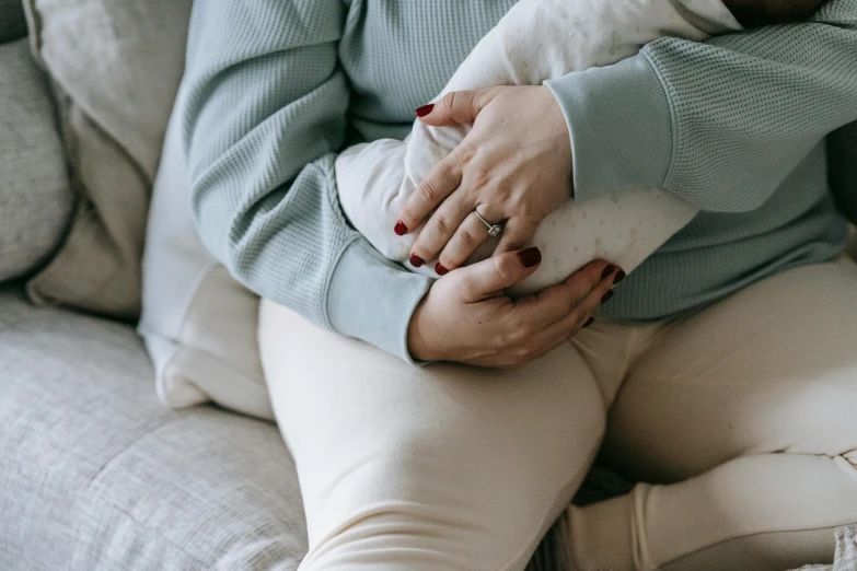 a woman sitting on a couch holding a baby, by Emma Andijewska, trending on pexels, swollen veins, folded arms, blue soft details, painful vibe