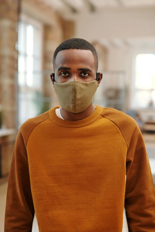 a man wearing a face mask standing in a room, ochre, unbeatable quality, frontal close up, muted brown