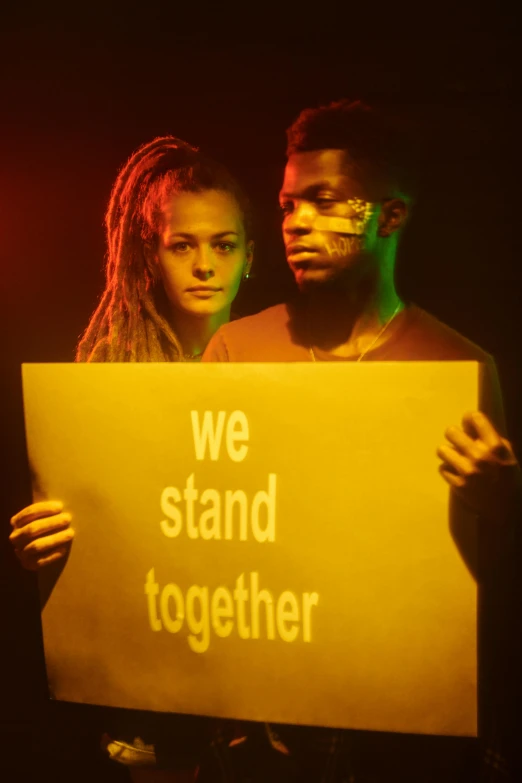 a man and woman holding a sign that says we stand together, an album cover, pexels, xxxtentacion, movie still, natgeo, coloured