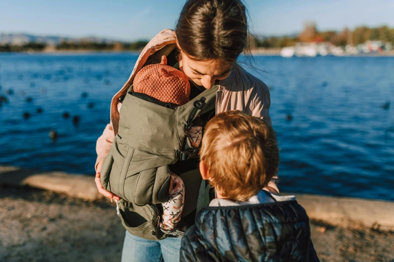 a woman holding a child near a body of water, a man wearing a backpack, sage green, quick assembly, thumbnail