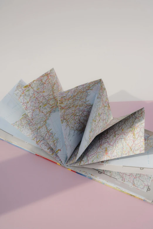 a folded book sitting on top of a pink surface, map, 3 d close - up, front facing view, traveller