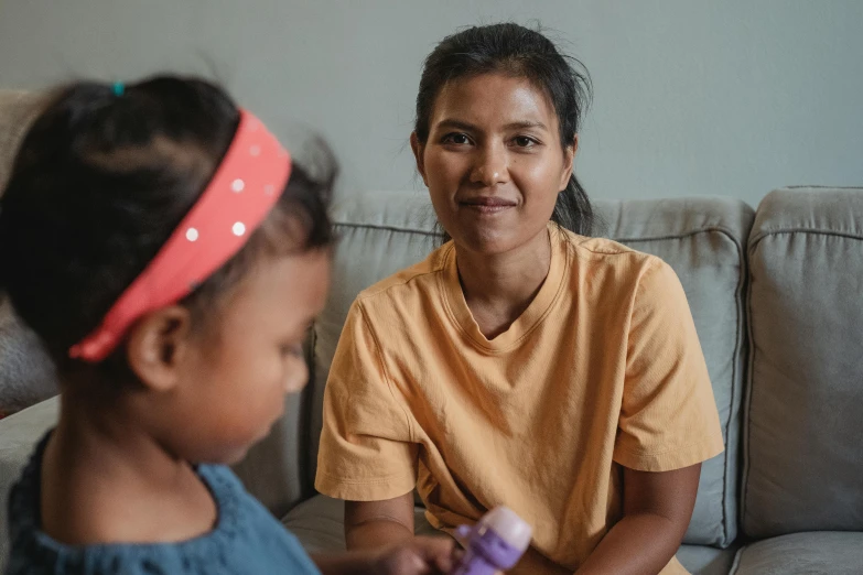 a woman sitting on a couch next to a little girl, pexels contest winner, hurufiyya, healthcare worker, south east asian with round face, avatar image, aboriginal capirote