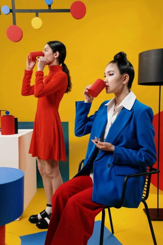 a woman sitting on top of a chair next to a woman in a red dress, inspired by Gao Cen, trending on pexels, pop art, celebration of coffee products, wearing a colorful men's suit, blue mood, lookbook