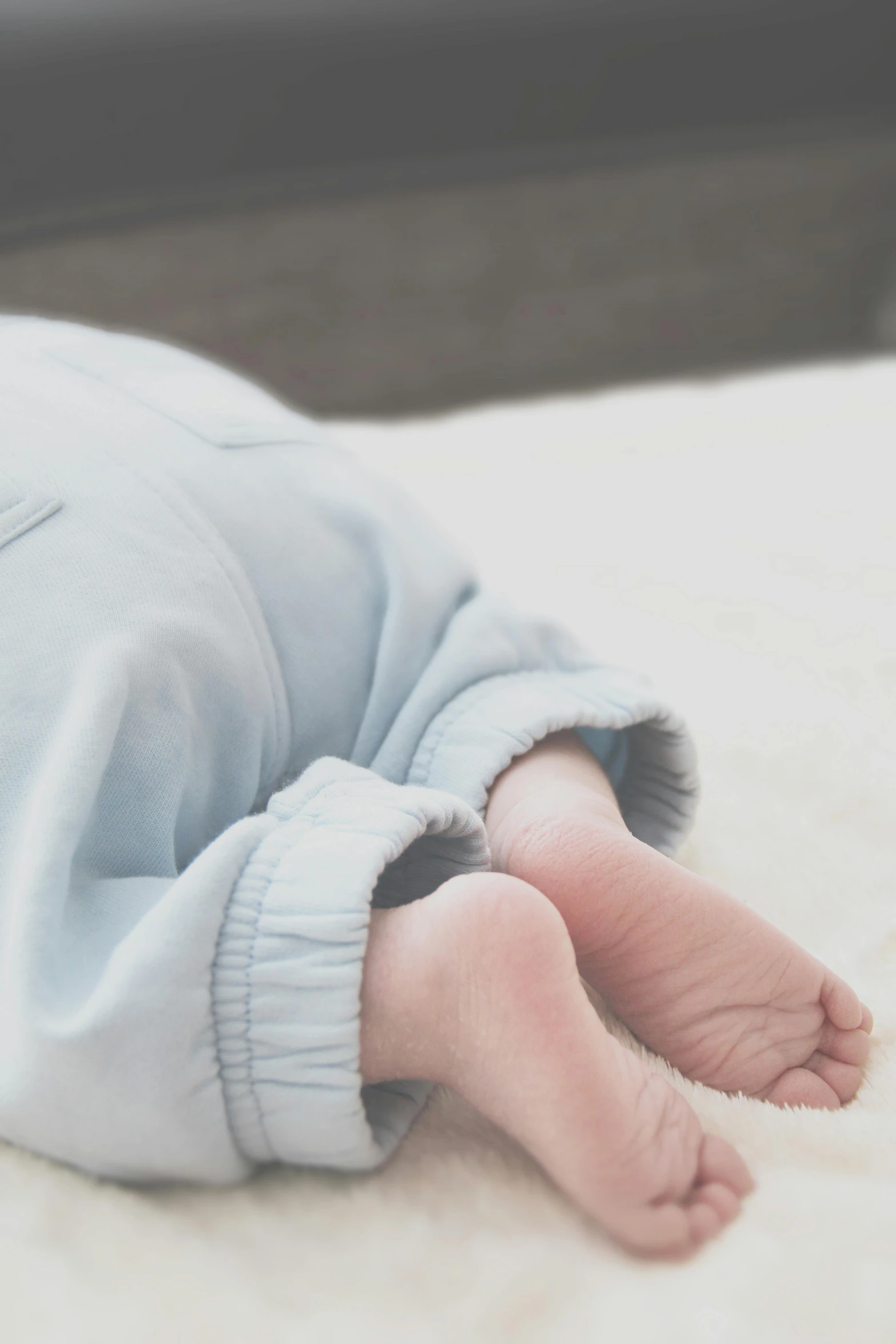 a close up of a baby laying on a bed, by Ruth Simpson, unsplash, happening, pale cyan and grey fabric, pants, about to step on you, looking down