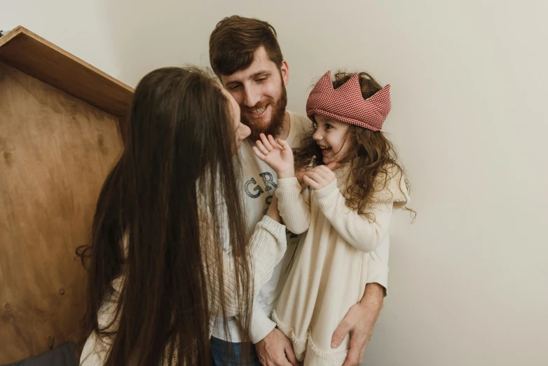 a man standing next to a little girl on top of a bed, by Emma Andijewska, pexels contest winner, queen crown on top of her head, beanie, happy family, bearded