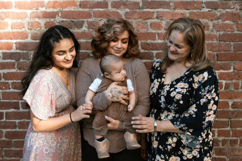 three women holding a baby in front of a brick wall, unsplash, hispanic, background image, lightly dressed, plus-sized