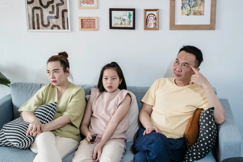 a group of people sitting on top of a blue couch, a cartoon, inspired by Zhang Xiaogang, pexels, portrait of family of three, annoyed expression, an indonesian family portrait, tv series