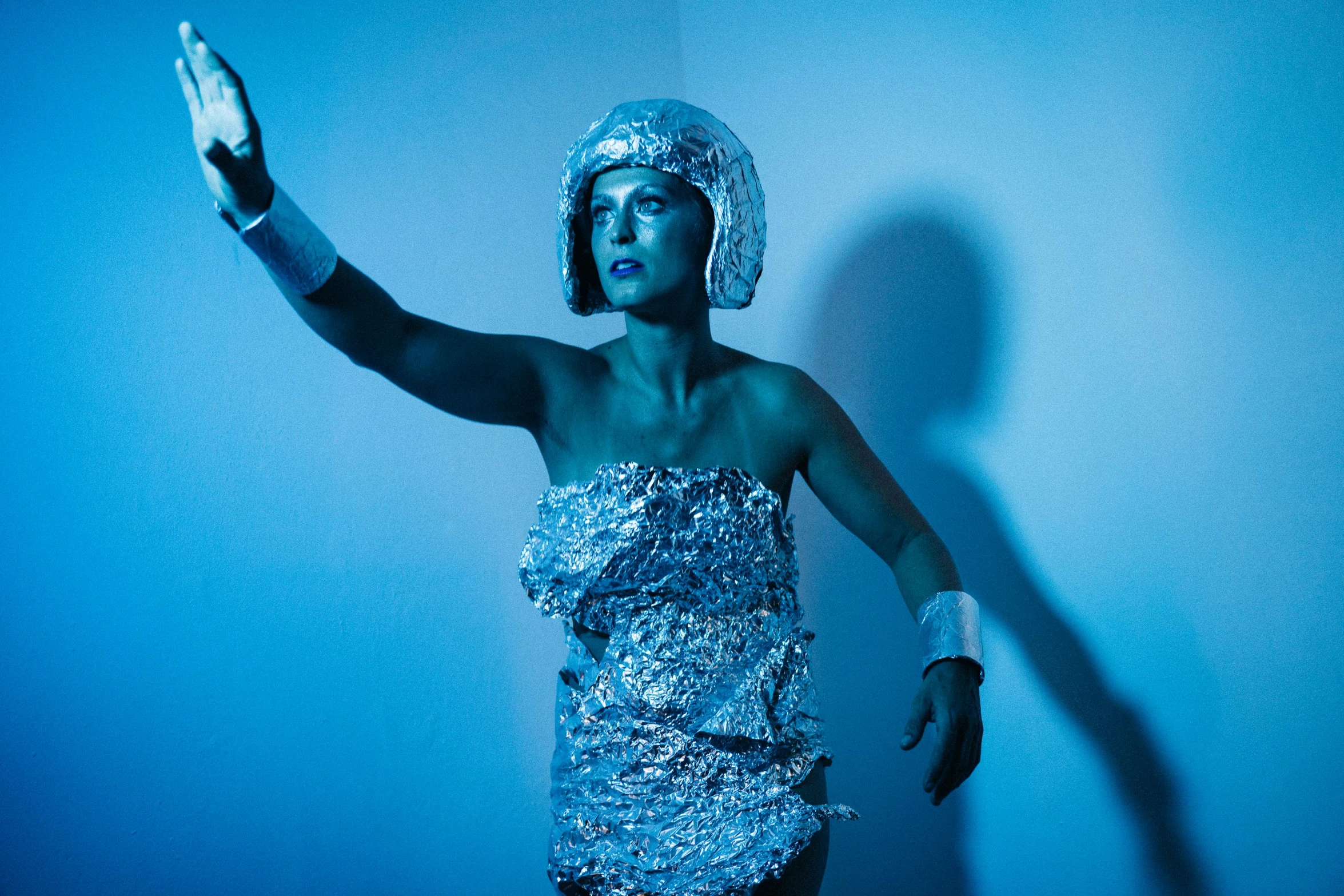 a woman in a silver dress posing for a picture, inspired by Cindy Sherman, unsplash, holography, in a space cadet outfit, dramatic white and blue lighting, covered in bandages, scrap metal headdress