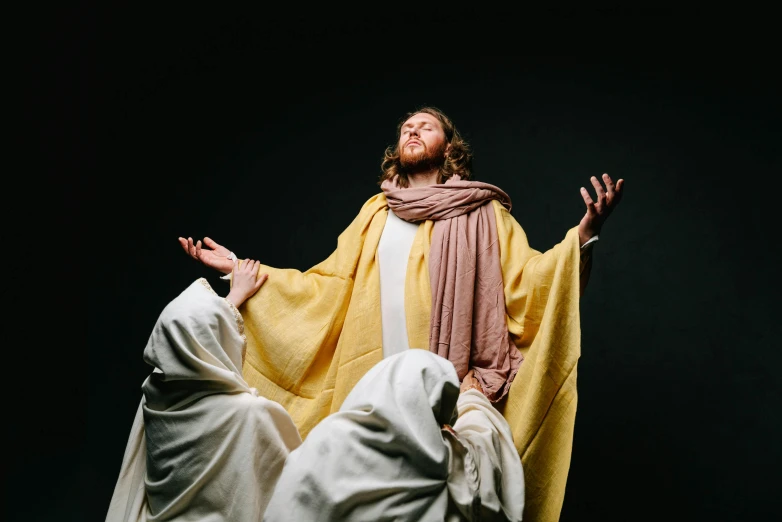 a man standing in front of a statue of jesus, by Everett Warner, unsplash, renaissance, yellow robes, ( ( theatrical ) ), ascension, the three moiras