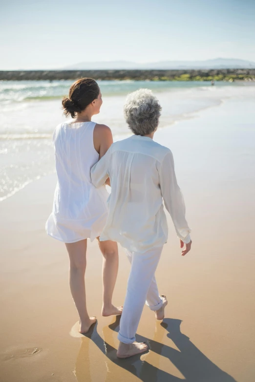 a couple of women walking on top of a sandy beach, older woman, bright white light, linen, stepping stones