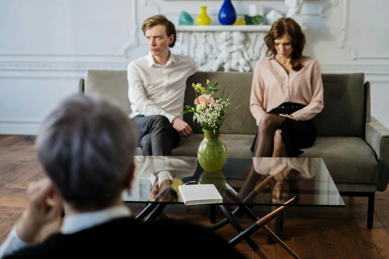 a man and a woman sitting on a couch in a living room, court session images, man sitting facing away, digital image