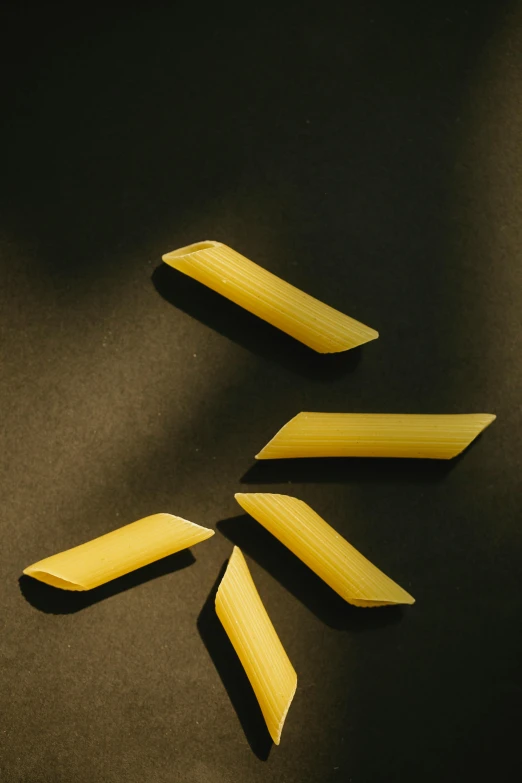 four pieces of pasta laid out on a black surface, a picture, inspired by Lucio Fontana, trending on pexels, yellow artificial lighting, translucent gills, detail shot, sleek spines