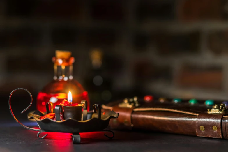 a leather case sitting on top of a table next to a lit candle, a still life, unsplash, renaissance, schnapps, pirate weapons, red and obsidian neon, on a candle holder