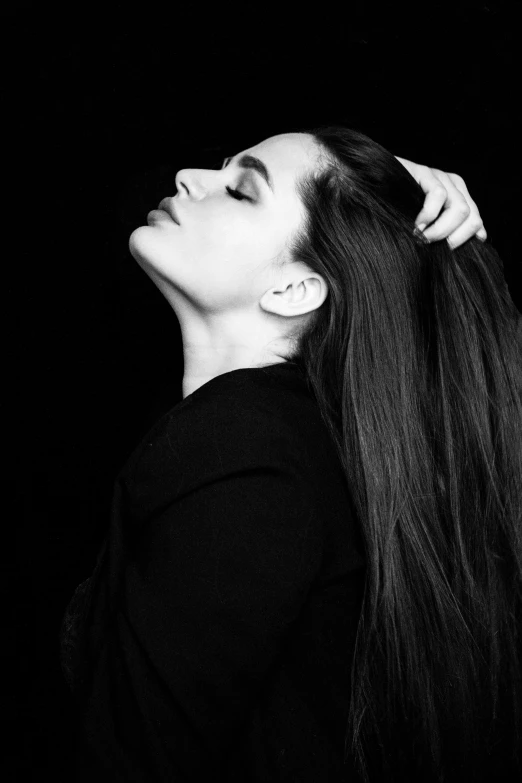 a black and white photo of a woman with long hair, profile pose, slicked-back hair, epk, hands in her hair