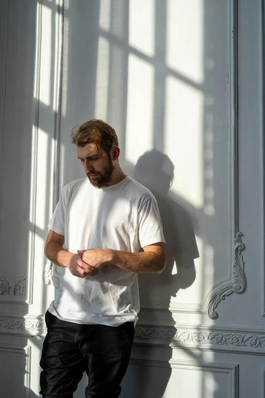 a man in a white shirt leaning against a wall, an album cover, inspired by Adam Pijnacker, pexels contest winner, light beard, standing in corner of room, play of light, actor liam hemsworth