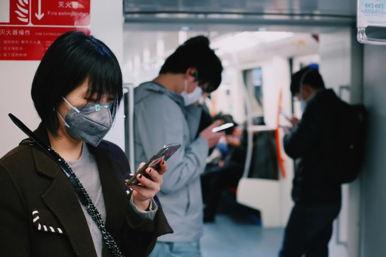 a group of people standing next to each other on a subway, trending on pexels, happening, chinese text, medical mask, she is holding a smartphone, platforms