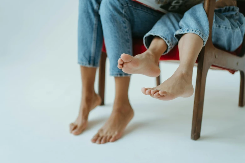 a person sitting in a chair reading a book, by Matija Jama, pexels contest winner, hyperrealism, barefeet, with a kid, close together, plain background