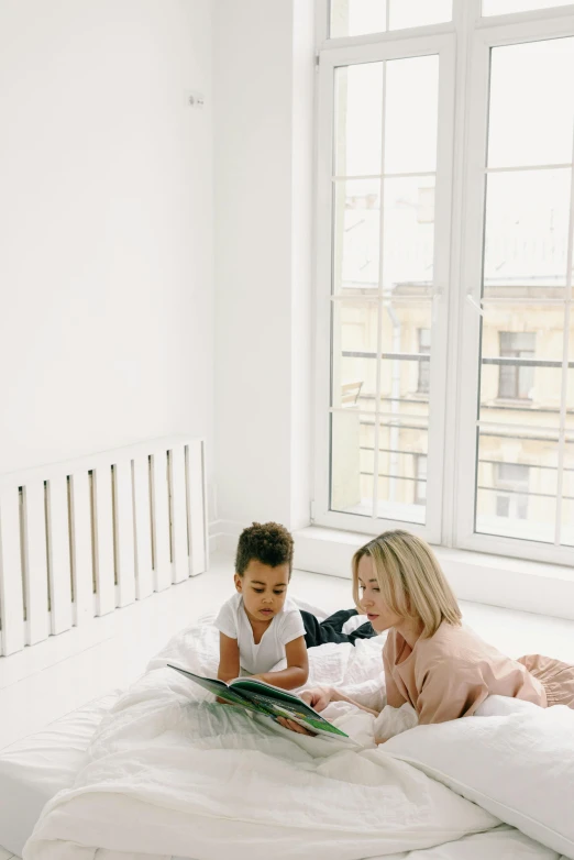 a woman and a child reading a book on a bed, pexels contest winner, in a white room, dwell, looking left, comicbook