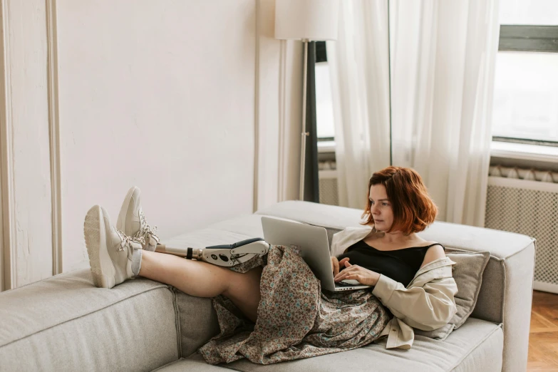 a woman sitting on a couch using a laptop, a portrait, trending on pexels, figuration libre, redhead girl, legs intertwined, wearing a grey robe, people watching around