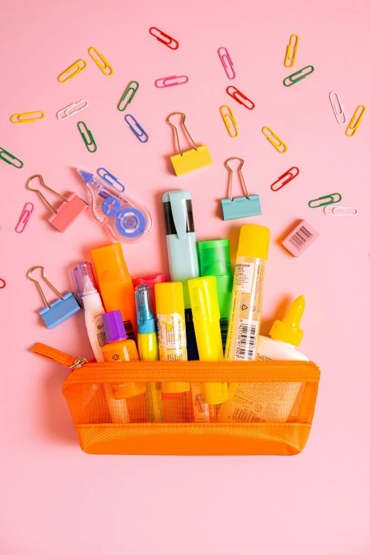 a basket full of school supplies on a pink background, in front of an orange background, colorful accents, in plastic, staples