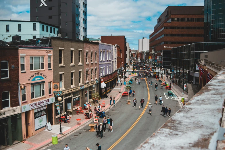 a group of people walking down a street next to tall buildings, by Washington Allston, pexels contest winner, aerial view of a city, walton's five and dime, quebec, thumbnail