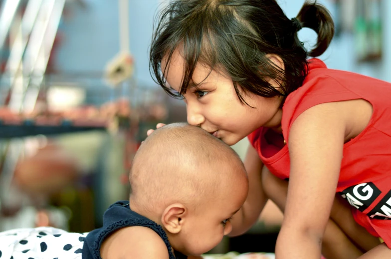 a couple of young children sitting on top of a bed, by Judith Gutierrez, pexels contest winner, indian girl with brown skin, close up shot from the side, nursing, center focus