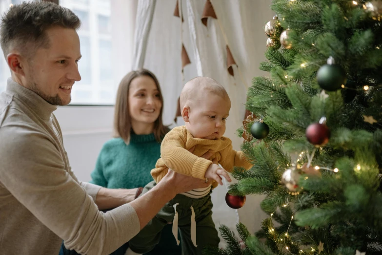 a man holding a baby in front of a christmas tree, pexels contest winner, manuka, avatar image, ornamentation, husband wife and son