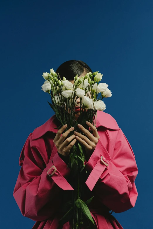 a woman holding a bunch of flowers in front of her face, an album cover, unsplash, aestheticism, girl in raincoat, bella poarch, blue skies, margiela campaign