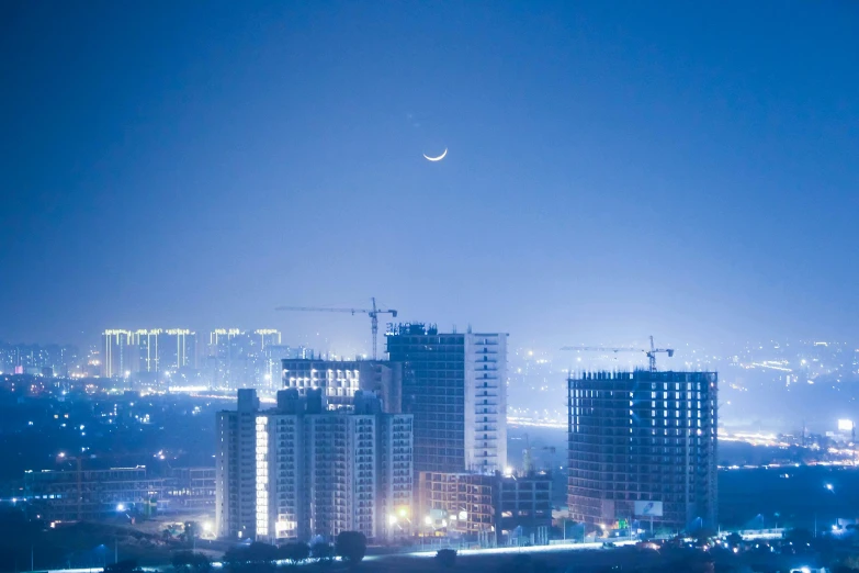 a view of a city at night with the moon in the sky, pexels contest winner, beautiful futuristic new delhi, tall thin build, blue, city mist softlight